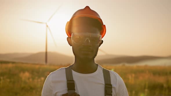 African American Man Standing on Field with Huge Windmills During Summer Sunset alt