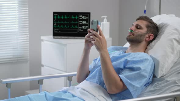 Man in Hospital with the Mobile Phone and Earphones Lying Alone in Bed alt