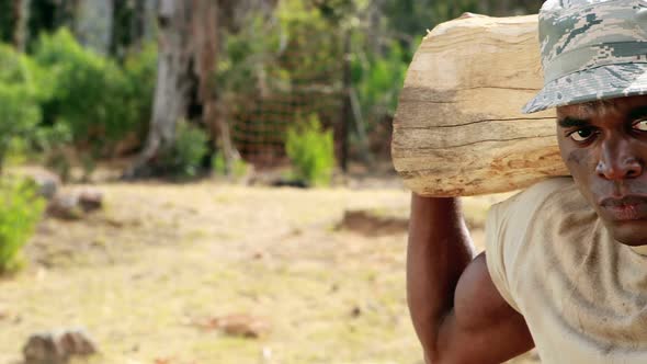 Fit man carrying heavy wooden log while exercising alt