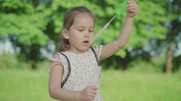 Close-up of Joyful Caucasian Girl with Brown Eyes Blowing Soap Bubbles and Talking. Charming alt