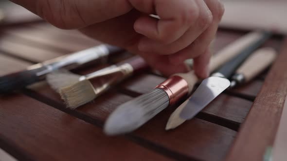 Closeup Female Hand Taking Round Painting Brush From Wooden Table alt