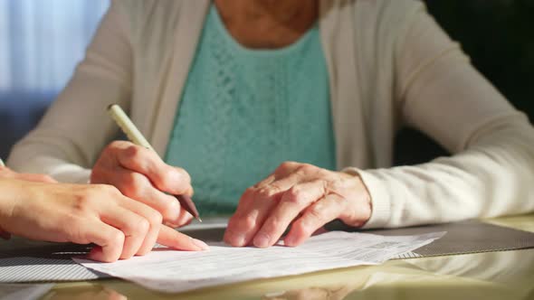 Hands of Volunteer Helping Senior Woman to Sign Document