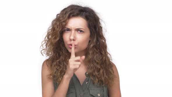 Serious Young Brunette Woman with Long Curly Hair in Casual Clothes Holding Index Finger on Lips alt