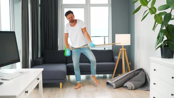 Man Fooling Around While Cleaning the House and Imagines Himself a Rock Star Plays the Broom Like a alt
