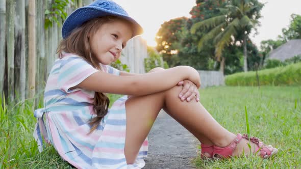 Happy Little Girl Sitting on the Grass and Playing in Summer Garden