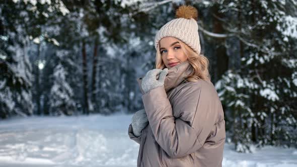 Happy Female in Hat Warm Jacket and Mittens Posing at Winter Forest alt