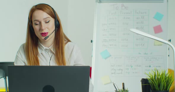 Woman in Headphones Talking To Students Via Video Conference at Empty Class alt