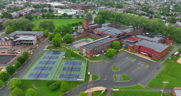 High aerial orbit around school. High school on wet, rainy, spring day in America. Tennis courts and alt