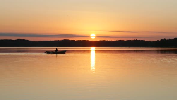 Sun Path on Water Surface and Man on Rowboat Crosses it at Sunset