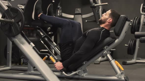 Side View of Young Man Exercising on Leg Press Machine in Gym  alt