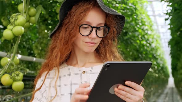 Young Woman Using or Playing Tablet in Greenhouse. Green Plant Growing in Warm House. alt