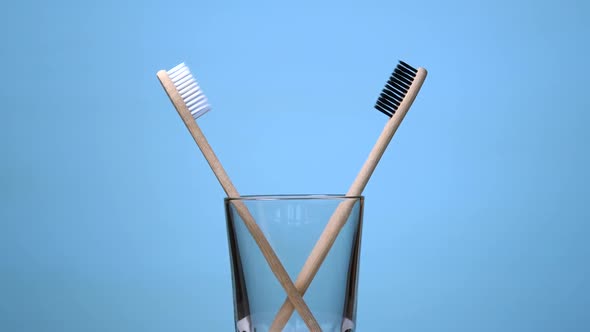 Bamboo Toothbrushes Rotating in Glass on Blue Background alt