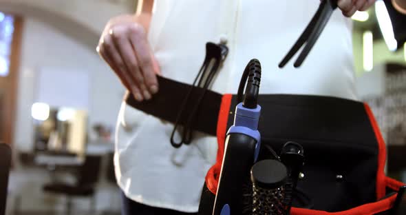 Mid-section of female hairdresser removing equipments from waist bag alt
