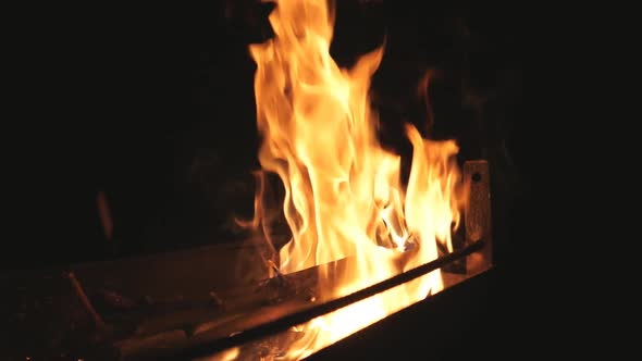 Red Flames Rises From Burning Slices Wood in Mangal on Black Background. Firewood Burns in Barbecue alt