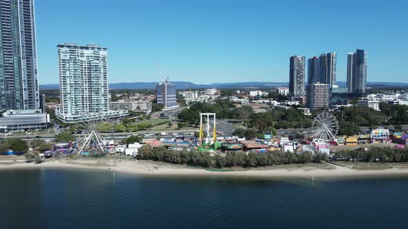 Oceanside carnival set-up along a coastal beach strip below a towering city landscape. Fast panning alt