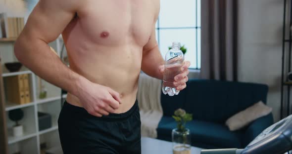 Sporty Man with Naked Torso Jogging on Running Track During Morning Home Workout and Drinking water alt