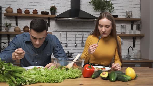 Cooking Salad at Home Young Vegetarians Eating Salad While Sitting in Modern Kitchen alt