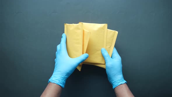 Hand in Latex Gloves Holding White Paper Bubble Envelope for Postal Ship alt