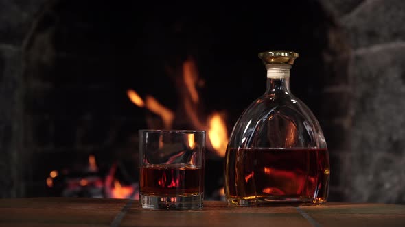 Bottle and Glass with Whiskey or Cognac on the Background of Fire in the Fireplace alt