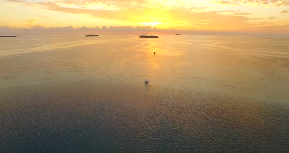 Aerial drone view of a man and woman having dinner on a floating raft boat at sunset. alt