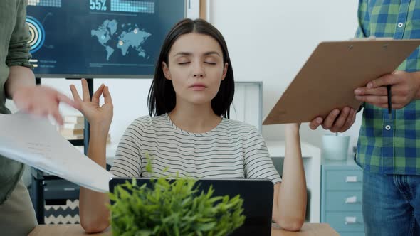 Beautiful Young Woman Meditating in Office with Eyes Closed While Colleagues Talking and Bringing alt
