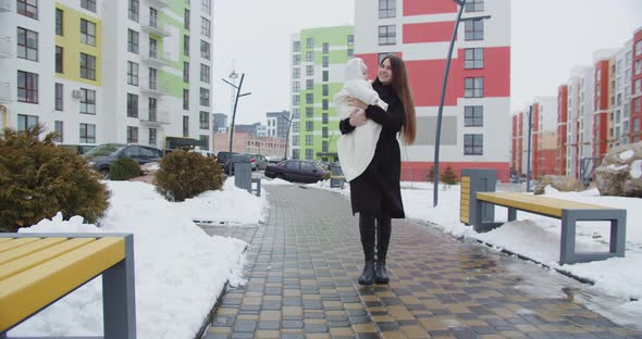 Loving Mother Walks Down The Street In Winter, Holding A Baby
