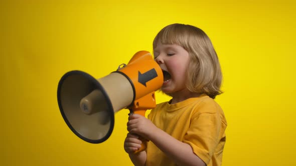 Little Cute Girl is Creaming in a Megaphone on the Yellow Background Studio alt