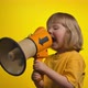 Little Cute Girl is Creaming in a Megaphone on the Yellow Background Studio