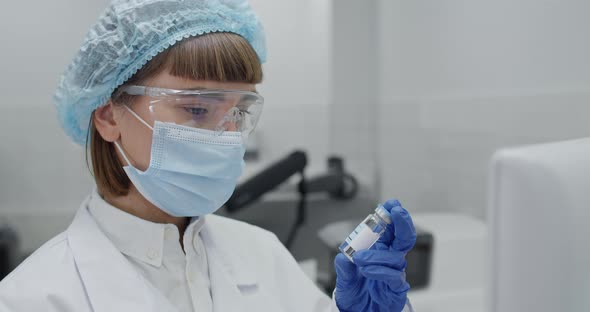 Close Up View of Female Worker in Protective Mask and Googles Entering Data on Computer alt