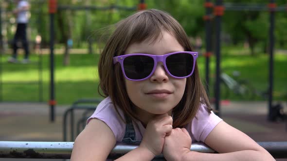 Little girl in sunglasses on a background of greenery