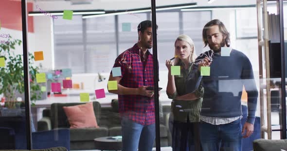 Diverse office colleagues writing on glass board and discussing together at modern office alt