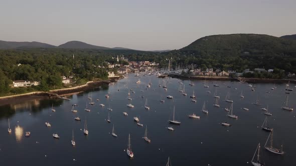 Aerial footage of an early morning flight over Camden harbor featuring many tall masted yachts and t alt