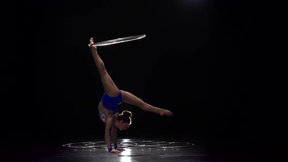 Gymnast in a Bright Outfit Twists a Hoop on Her Arm and Then on Her Leg alt