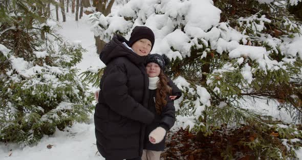 A Boy And A Girl Gently Hugging Near A Christmas Tree In The Snow. Children Play In The Yard