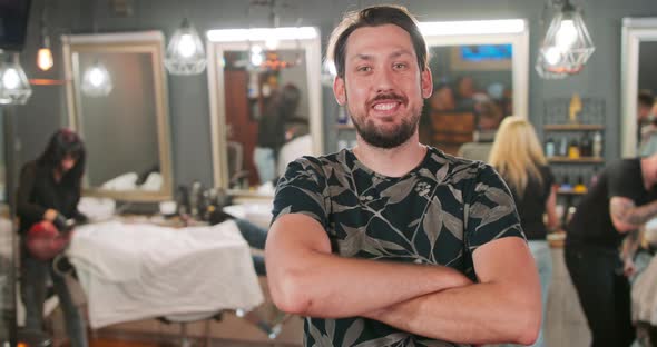 Young Bearded and Mustashed Man in Front of Camera Smiles Crossing His Arms Over His Chest in alt