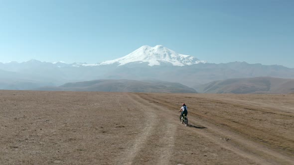 Woman Riding on Electro E-bike Bicycle at Mountain Plain on Snowy Peak and Valley Landscape From alt