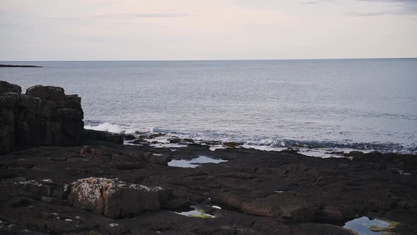 Beautiful waves splashing on the rocky shoreline of Dunstanburgh, England - wide shot alt