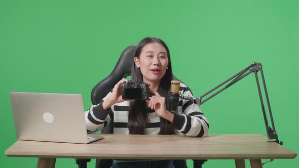 Asian Woman With Computer Reviewing Camera While Sitting In Front Of Green Screen alt