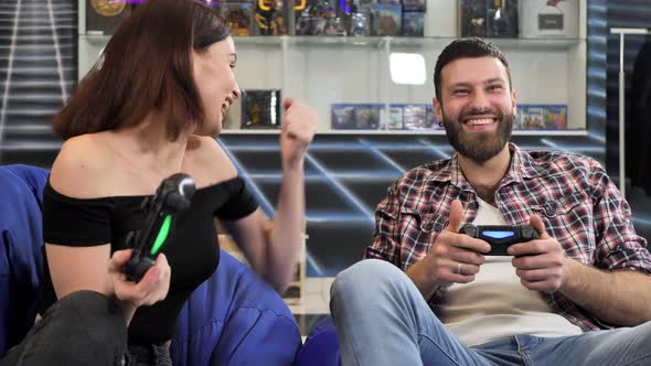 Young Couple Playing Video Games Sitting on Chairs in a Gaming Club with Controllers in Their Hands