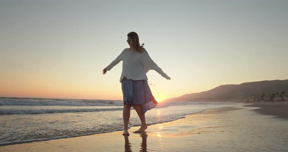 Happy Woman Having Fun on the Ocean Shore with Wind Blowing Her Hair and Dress alt
