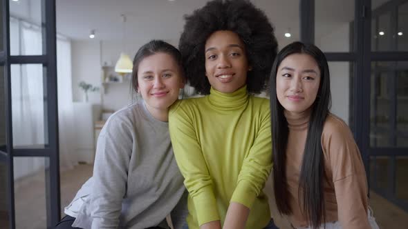Three Charming Multiethnic Young Women Posing Indoors Looking at Camera Smiling alt