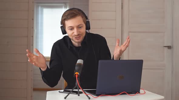 Young hipster man with headphones recording podcast using laptop at home studio alt