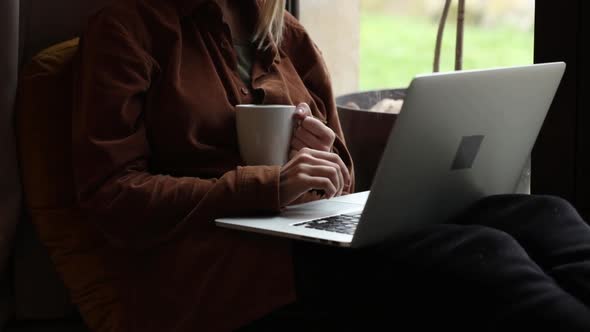 Woman with cup of coffee and  laptop computer near window