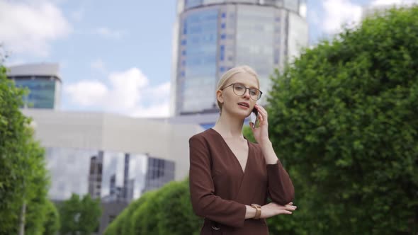 Young Business Woman Makes an Appointment By Phone Against the Backdrop of Skyscrapers