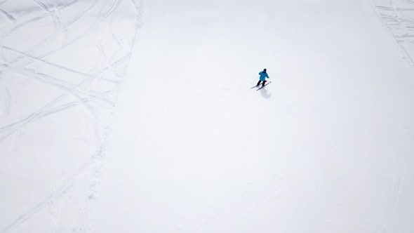 Aerial - Top view tracking shot of good alpine skier skiing down the wide ski slope alone. Sunny win alt