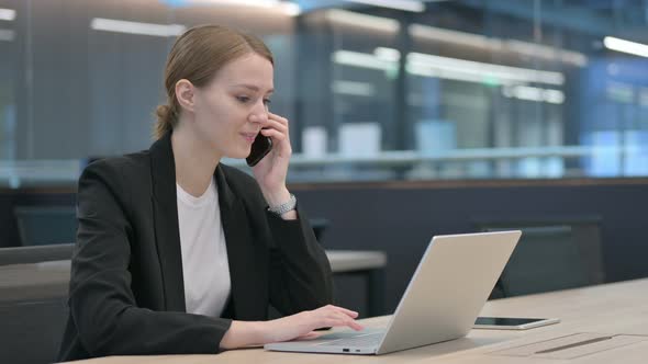 Businesswoman Talking on Smartphone While Using Laptop alt