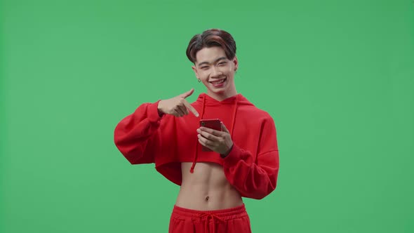 Smiling Asian Transgender Male Use Mobile Phone And Pointing To Smart Phone On Green Screen Studio alt