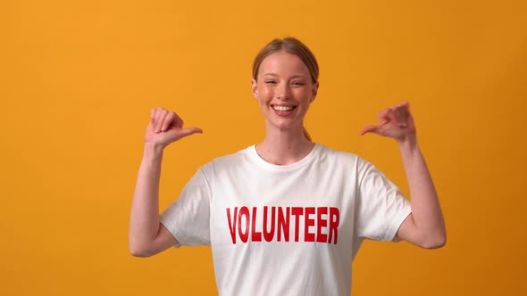 Smiling woman volunteer pointing at her t-shirt alt