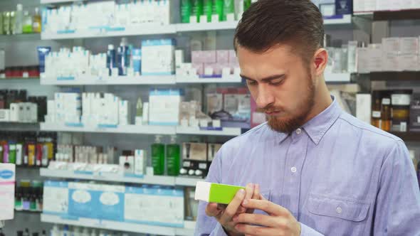 A Young Man Holds a Medicine in His Hand and Reads Something on the Phone  alt
