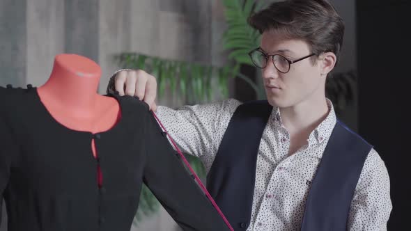 Portrait of Young Confident Designer Measuring Dress on Mannequin and Smiling at Camera. Brunette alt